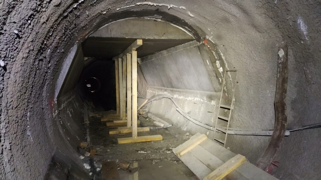 Underground tunnel under construction with wooden shoring and rough concrete walls.
