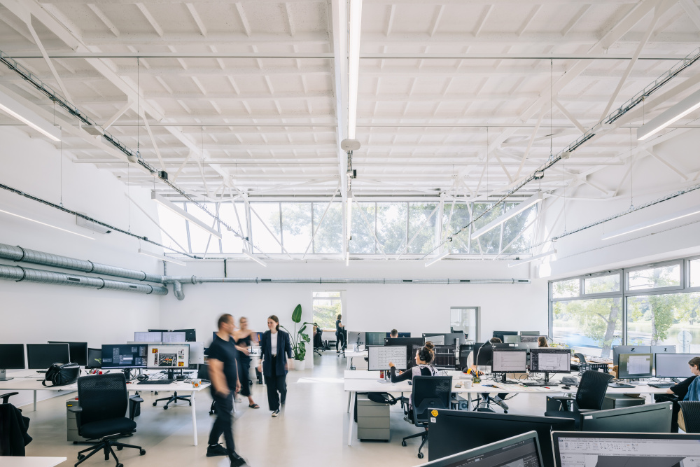 Open-plan office with rows of desks and computer monitors, employees at work in a bright, airy space.