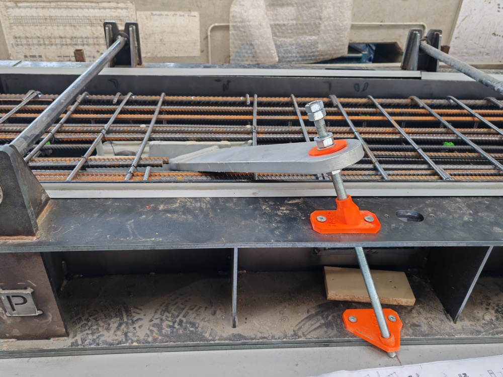 Industrial formwork with a steel rebar grid and orange adjustable clamps/bolts securing the frame.