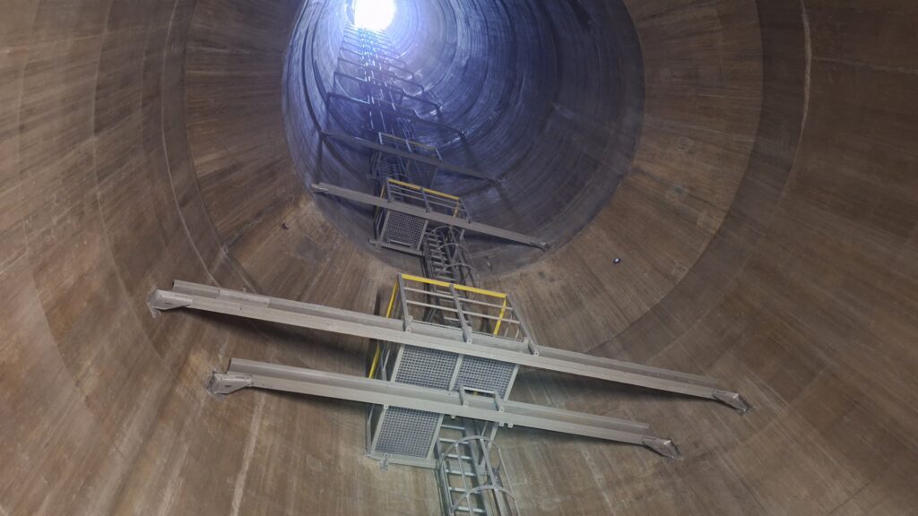 Interior view of a tall cylindrical shaft with metal staircases and platforms spiraling down.