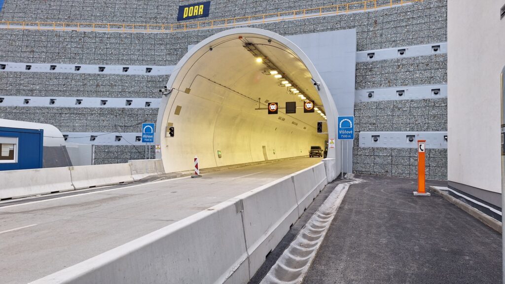Road tunnel opening into a rocky mountainside; interior lights visible and a car approaching inside.