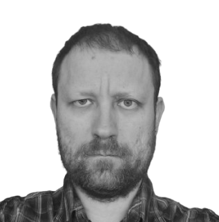 Portrait of a man with short hair and beard, wearing a plaid shirt, looking straight at the camera with a neutral expression.