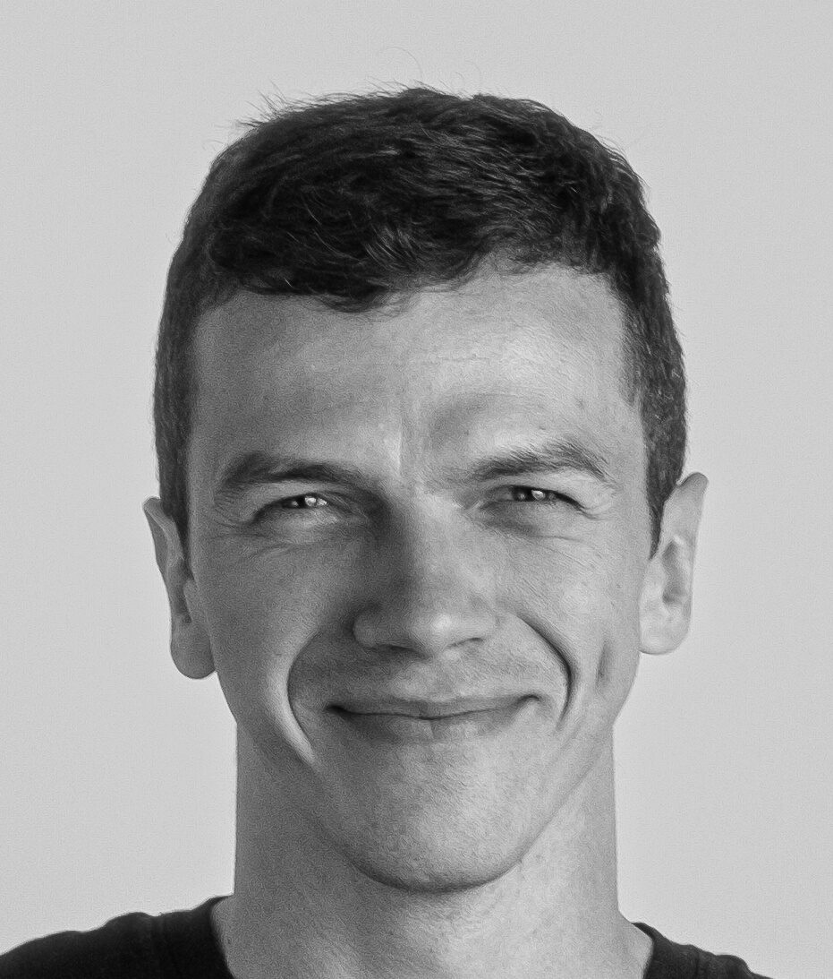 Close-up black-and-white portrait of a smiling man facing the camera.
