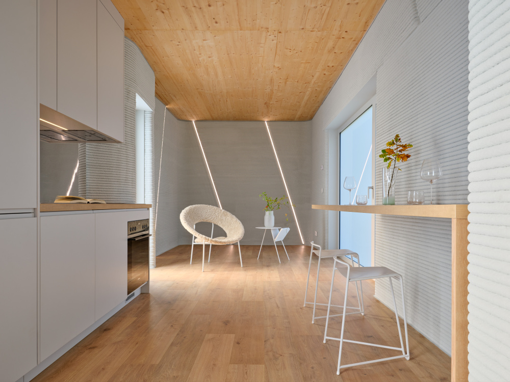 Open-plan kitchen and dining area with white cabinets, wooden floor and ceiling, and a high bar table with two white stools.